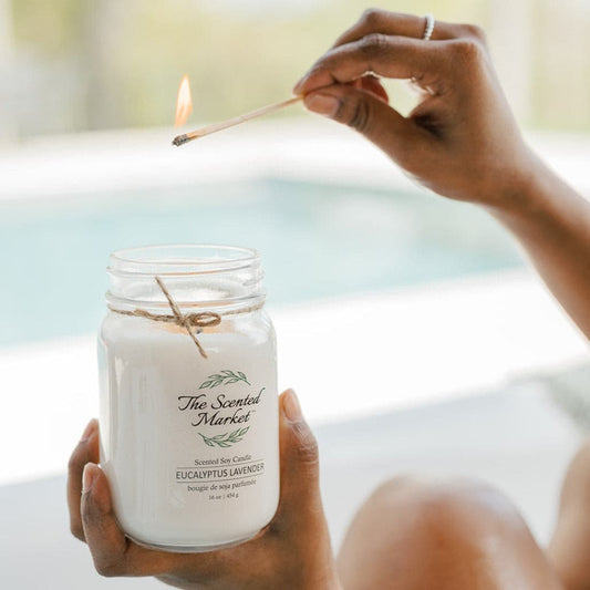 Person lighting a candle labeled 'The Scented Market' with a blurred background