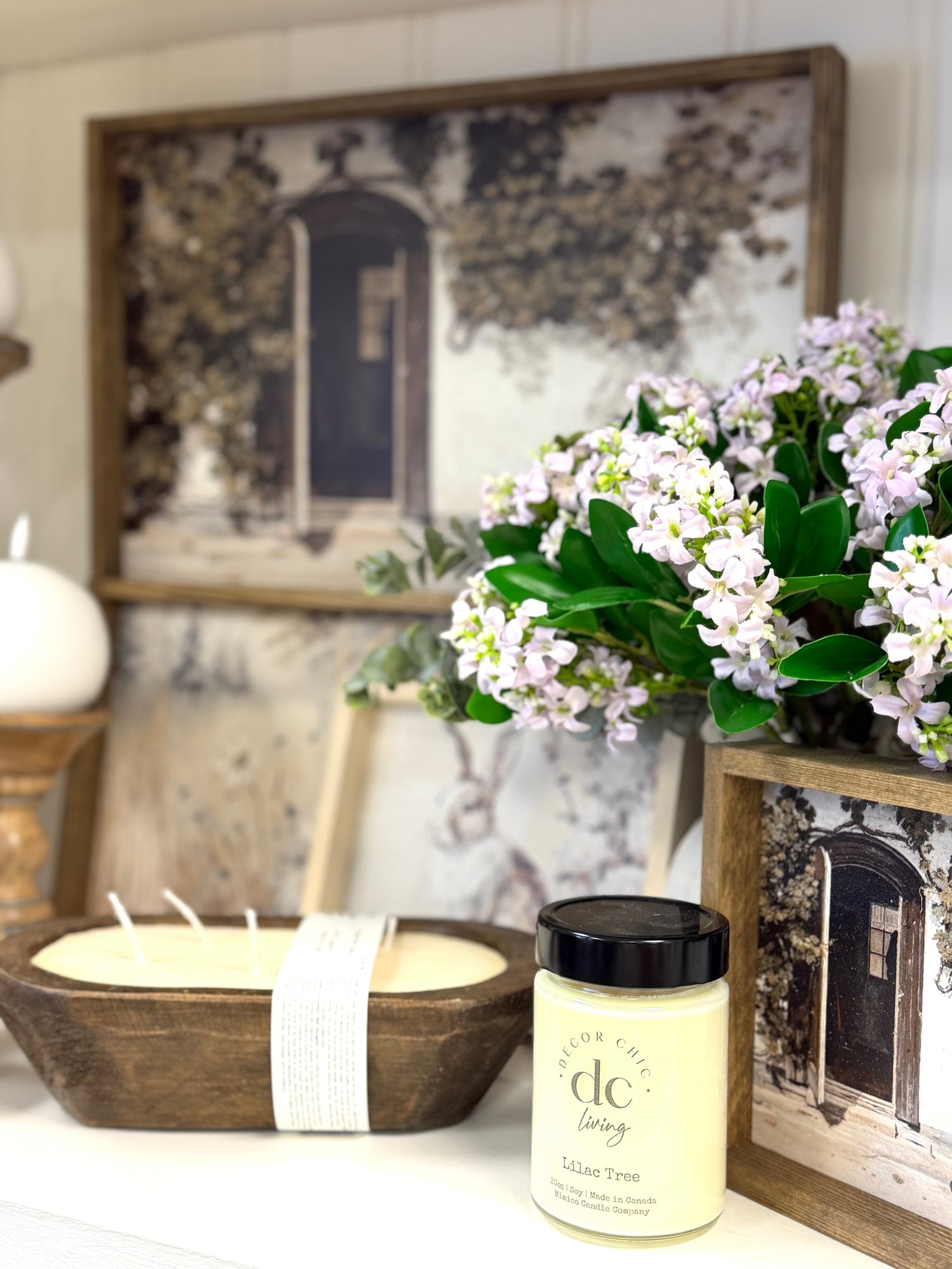 DecorChic Living Lilac Tree candle styled with faux lilac florals, wood bowl and framed home decor.