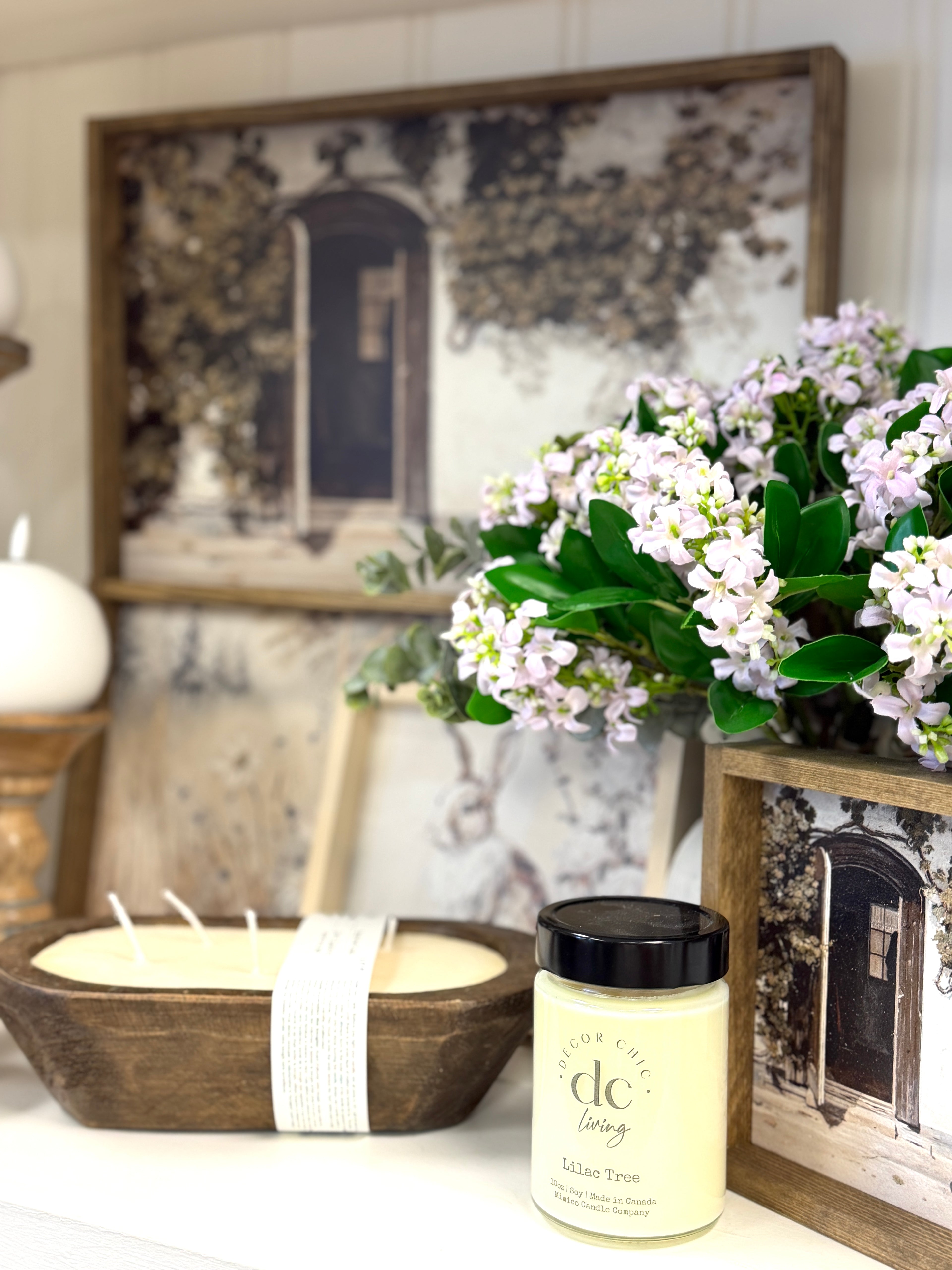 DecorChic Living Lilac Tree candle styled with faux lilac florals, wood bowl and framed home decor.