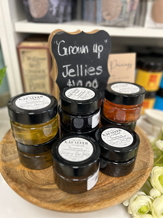 Jars of Kavaleer Jellies displayed on a wooden tray with a chalkboard sign in the background indicating the price.