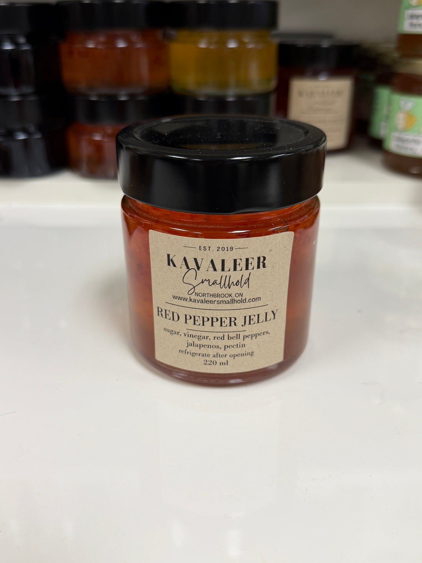 Jar of red pepper jelly with a label on a white surface