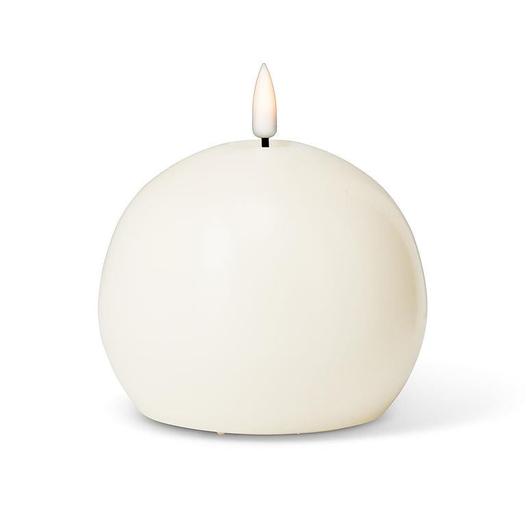 Sand spherical candle with a lit wick on a white background