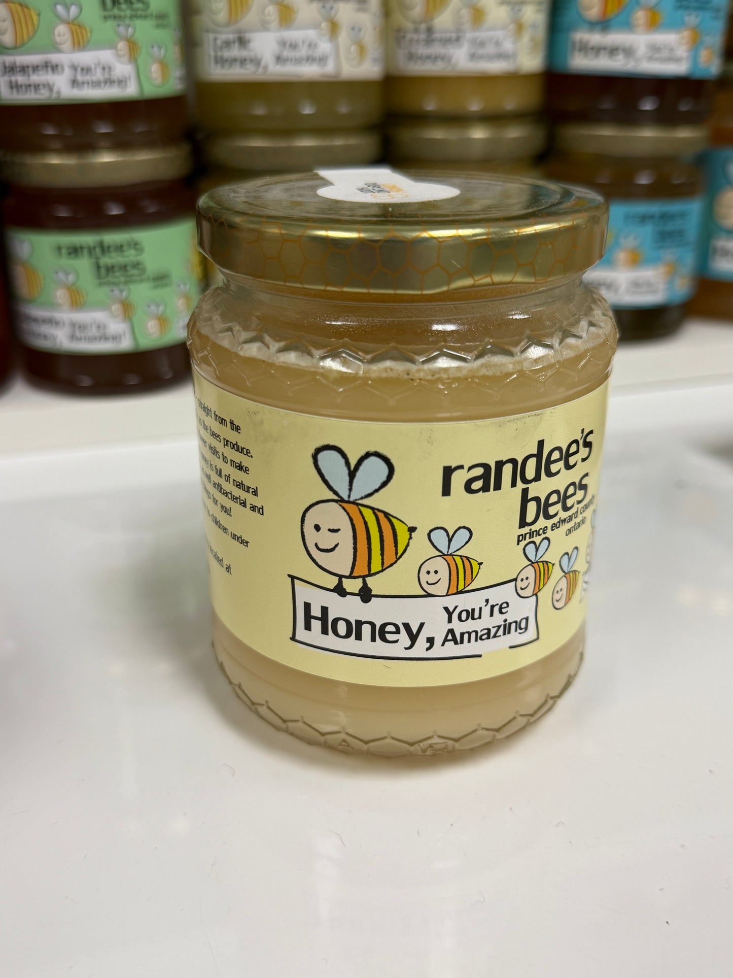 Jar of honey with a smiley bee design on a white surface