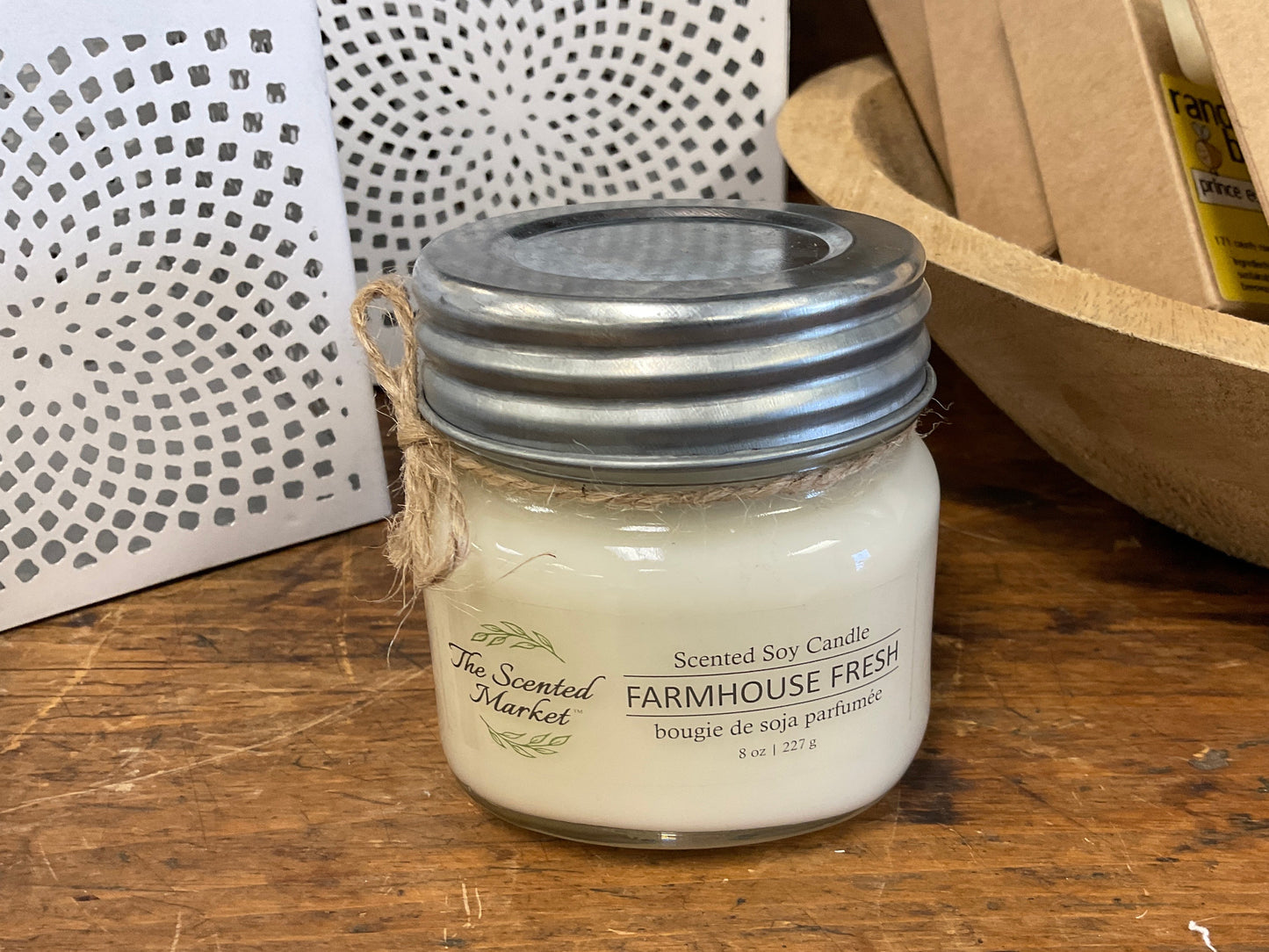 Jar candle labeled 'Farmhouse Fresh' on a wooden surface with a decorative background.