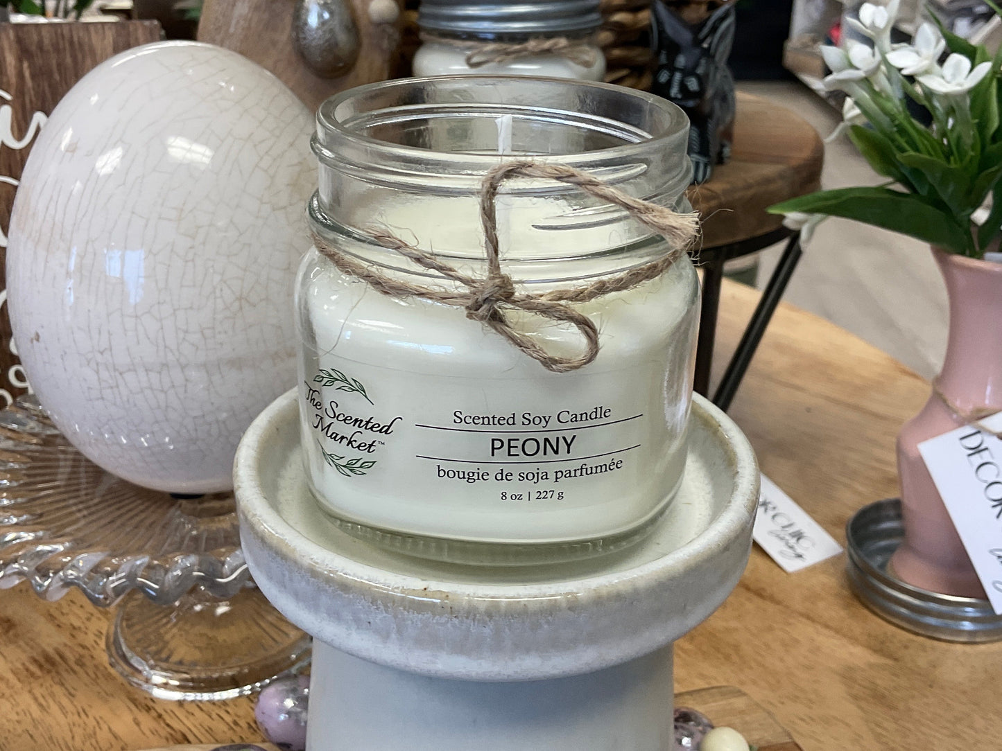 Scented soy candle in a glass jar on a decorative stand with a blurred store background