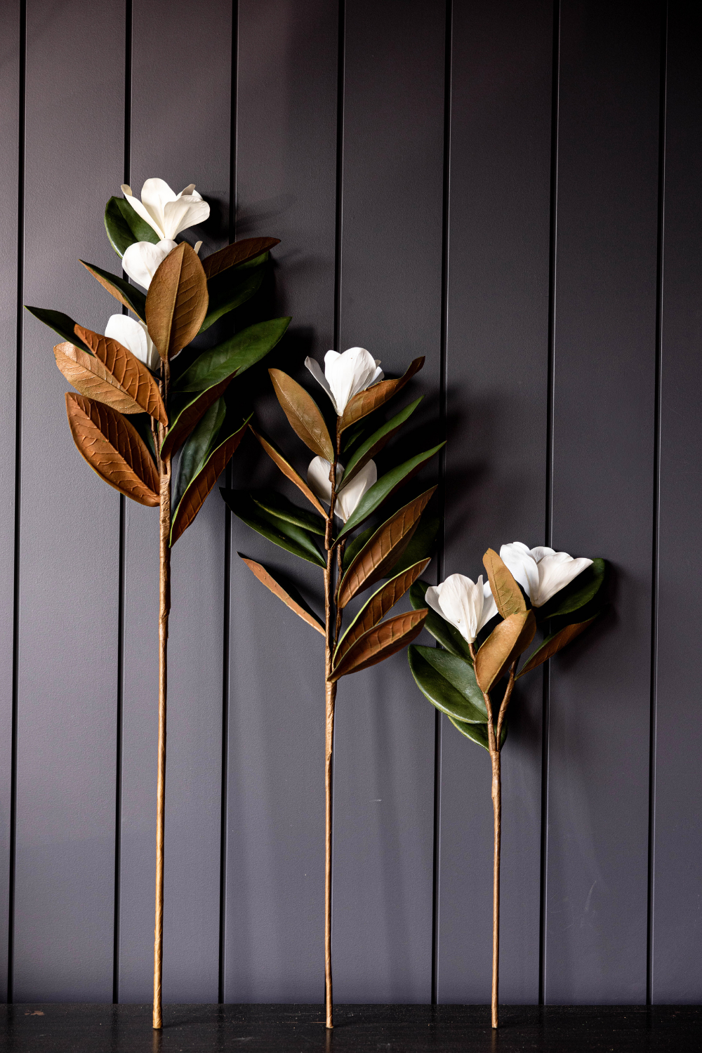 Small faux magnolia stems styled in a dark vase with white blooms and hand-painted leaves